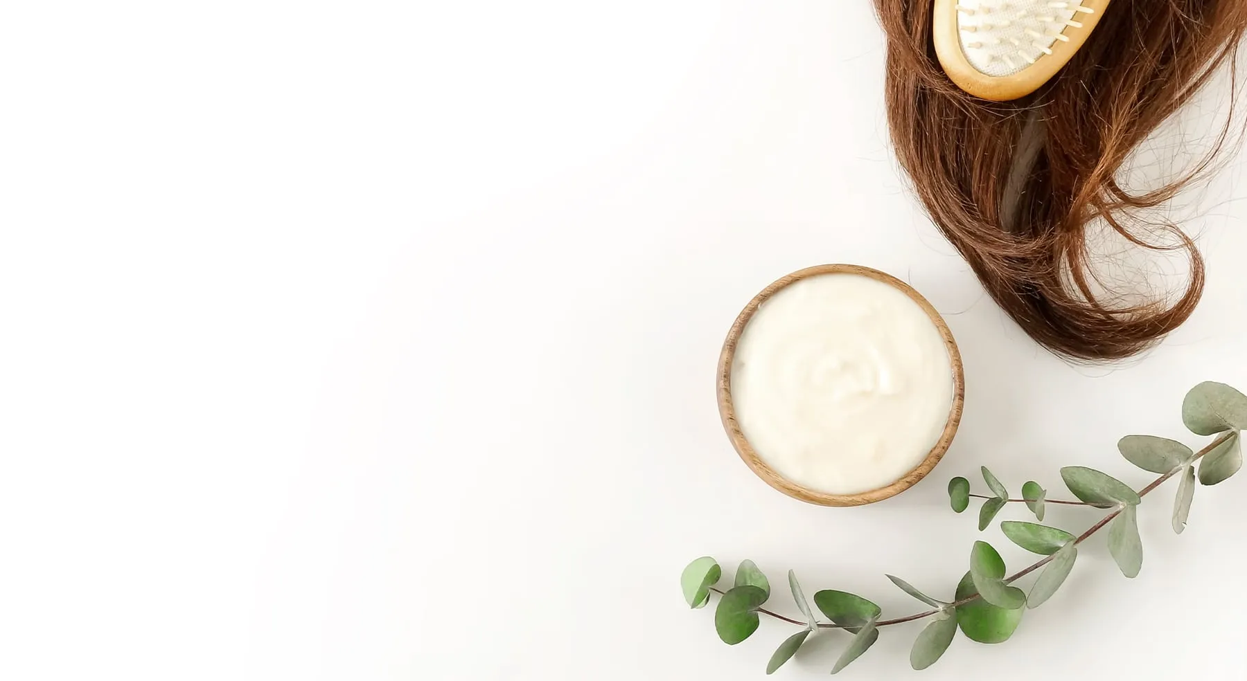 Hair mask in a bowl beside a lock of hair and eucalyptus
