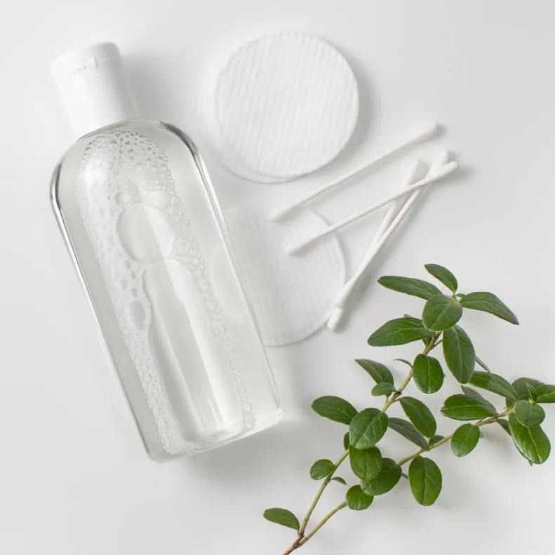 Clear bottle of cleansing water with cotton pads and mint